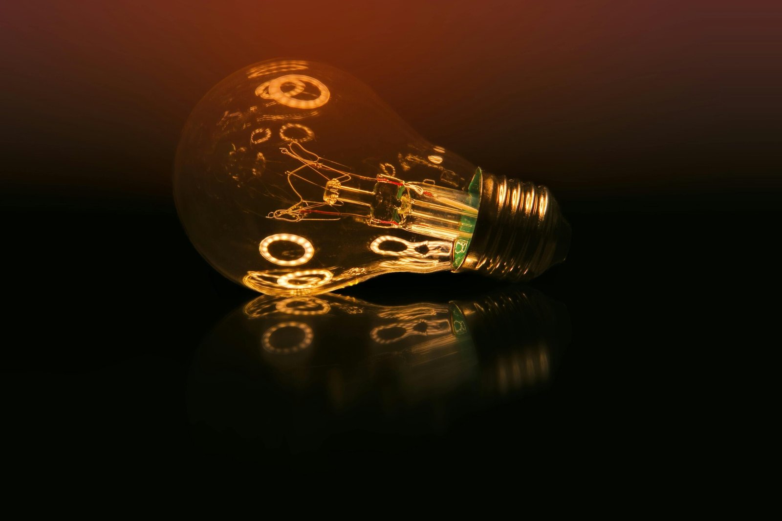 A glowing light bulb on a dark reflective surface creating a warm ambient atmosphere.
